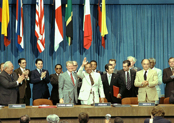 President Carter, Omar Torrijos, and other dignitaries stand and clap at a signing ceremony.