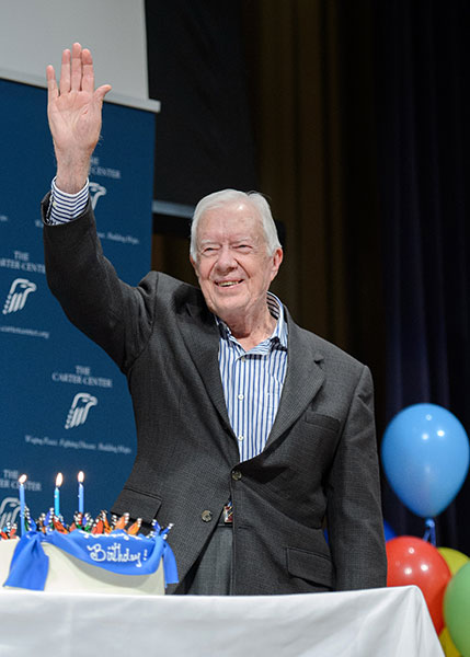 Jimmy Carter in front of a birthday cake, waving to attendees.