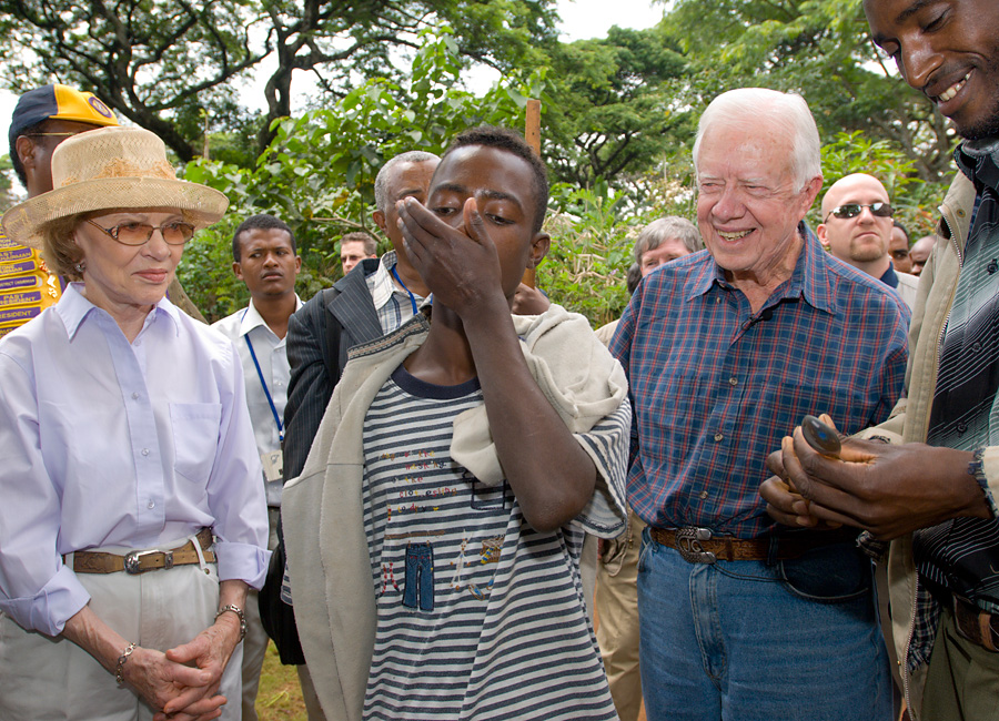 Jimmy and Rosalynn Carter watch as a male patient swallows medication.