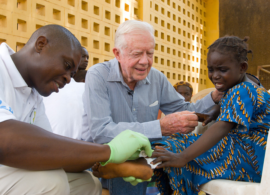 Jimmy Carter holding a young patient as a Guinea worm is removed from her body.