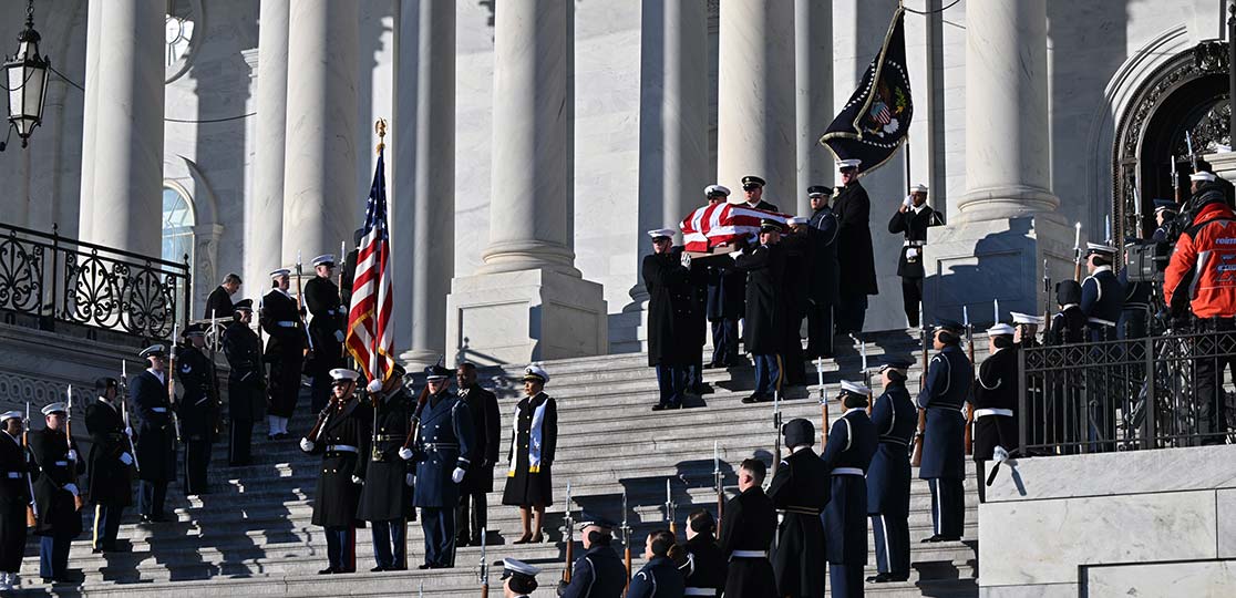 Military personnel carry flag-draped casket down stairs