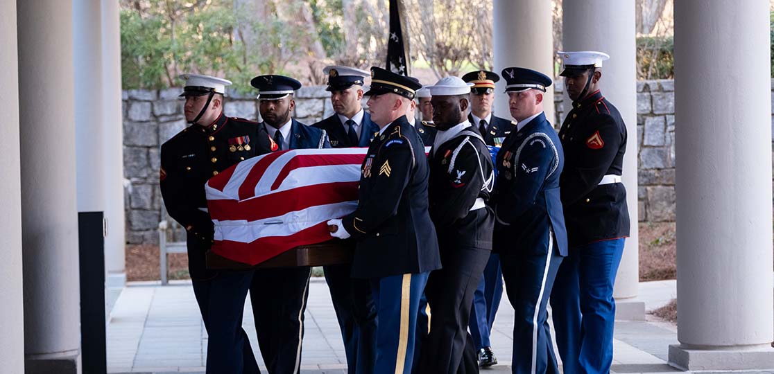 Military personnel carry flag-draped casket